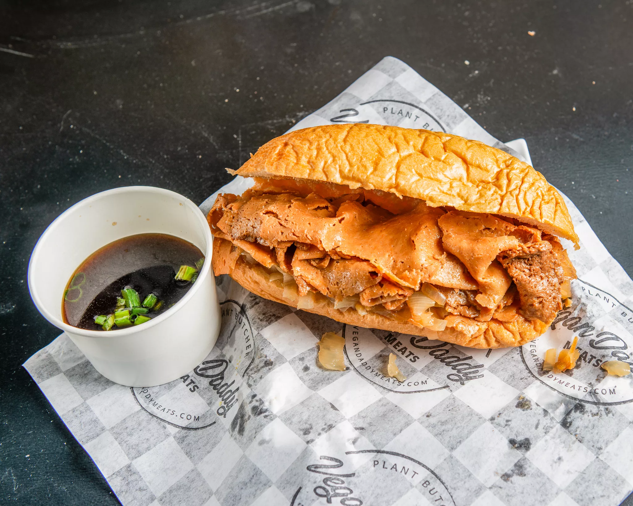 Sandwich with fried meat and sauce on a bun, served with soy sauce and green onion, on paper-lined tray.