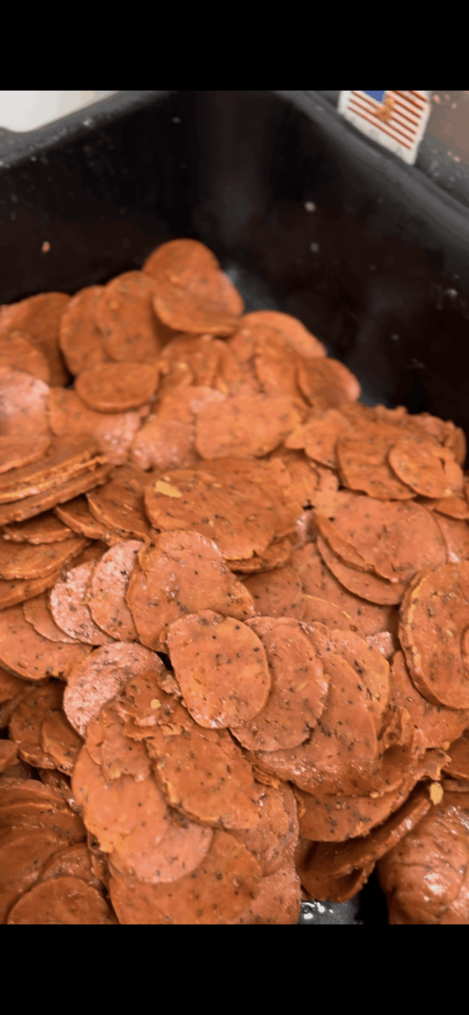 Pile of cooked sliced sausage in a black container, with some pieces overlapping.