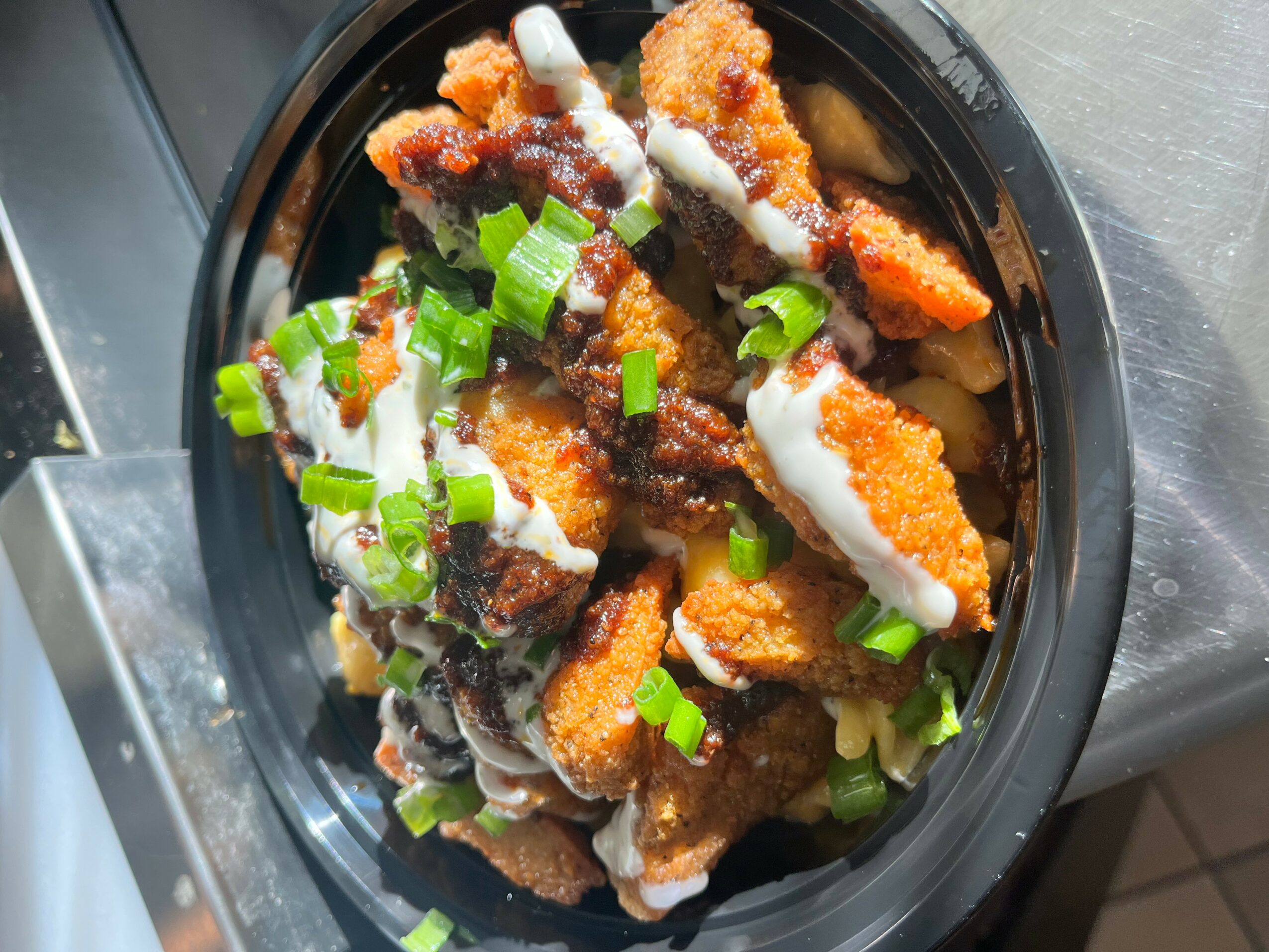 Fried chicken pieces topped with chopped green onions in a black bowl.
