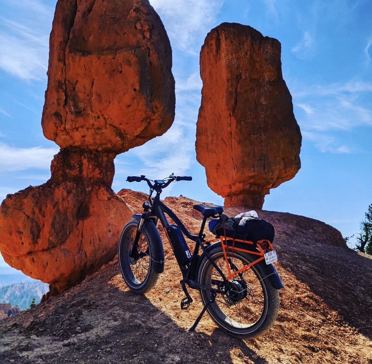 Bicycle parked on rocky terrain with two large balanced rocks in the background under a blue sky.