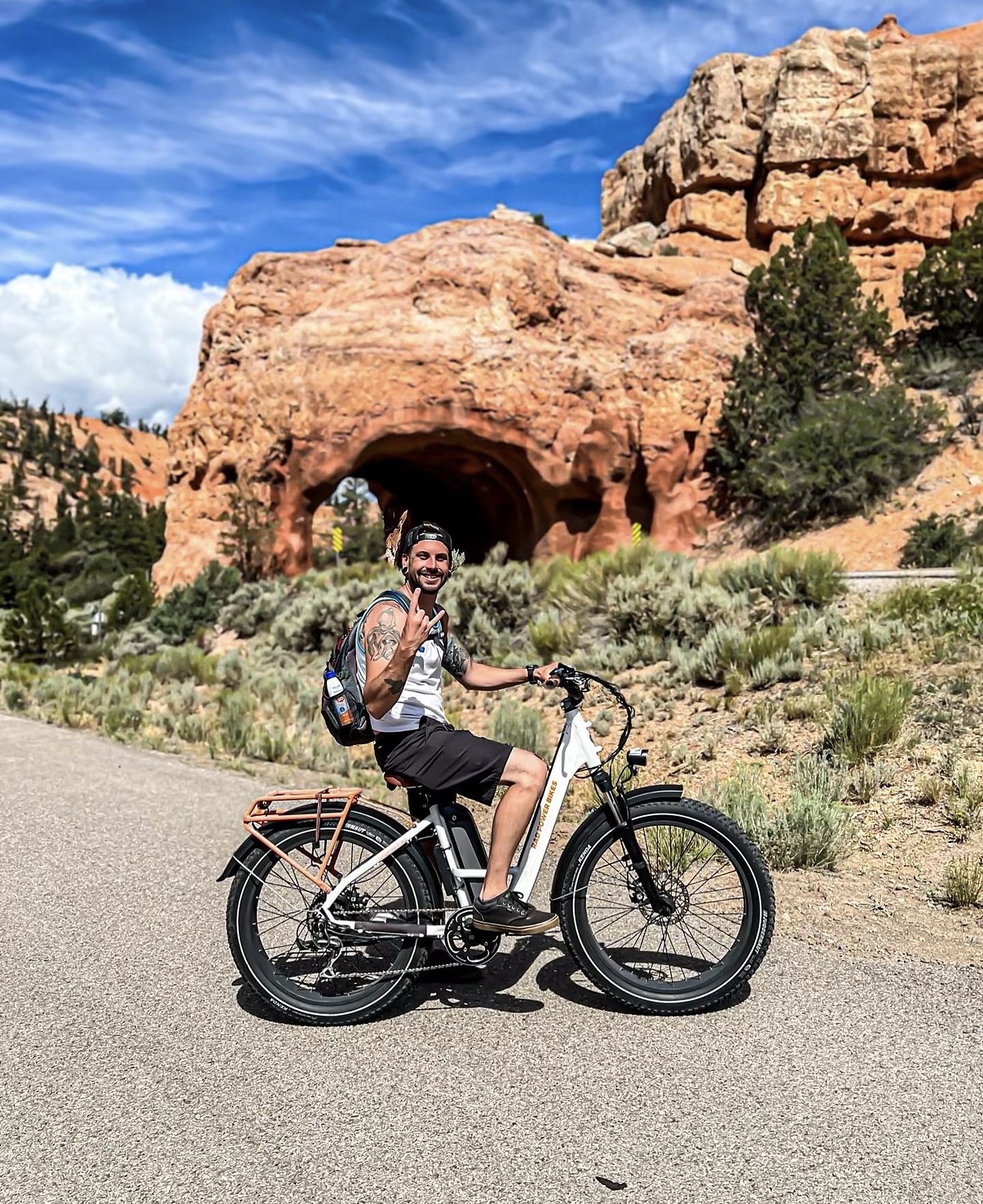 Person riding a bicycle on a road with a large rock formation and blue sky in the background.