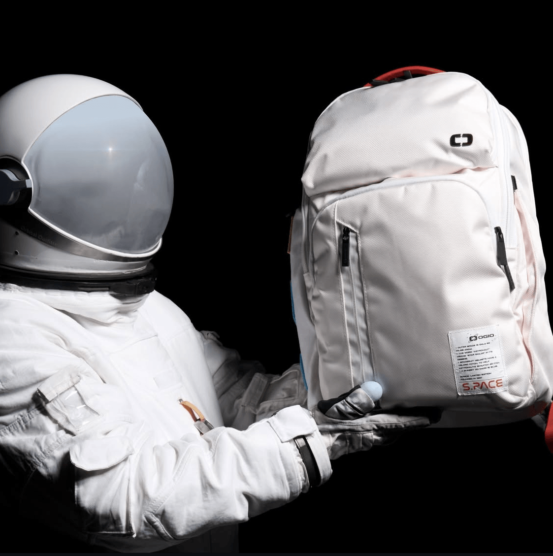 Person in astronaut suit holding a white backpack against a black background.