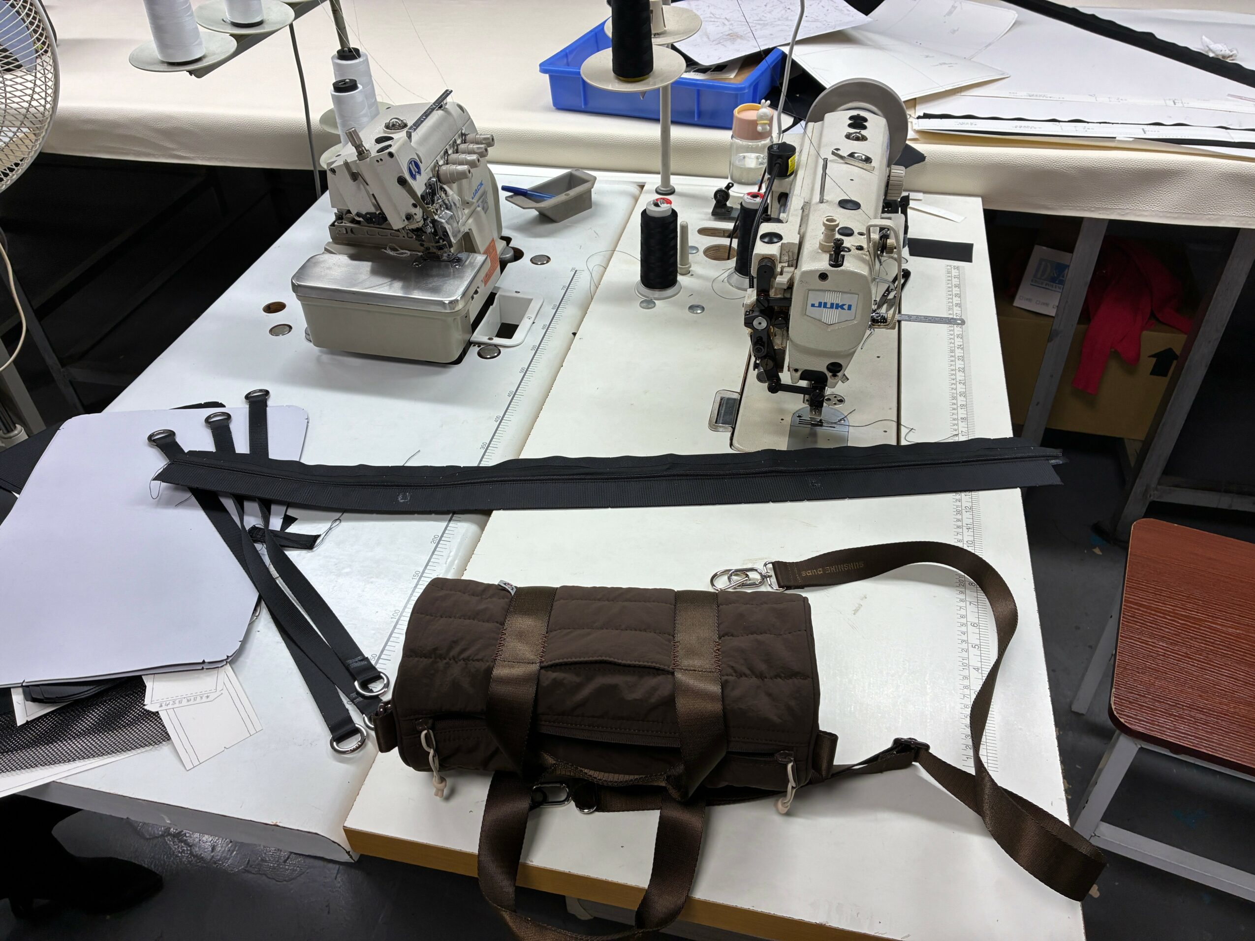 Workstation with sewing machines, fabric, and a brown bag on a white table.