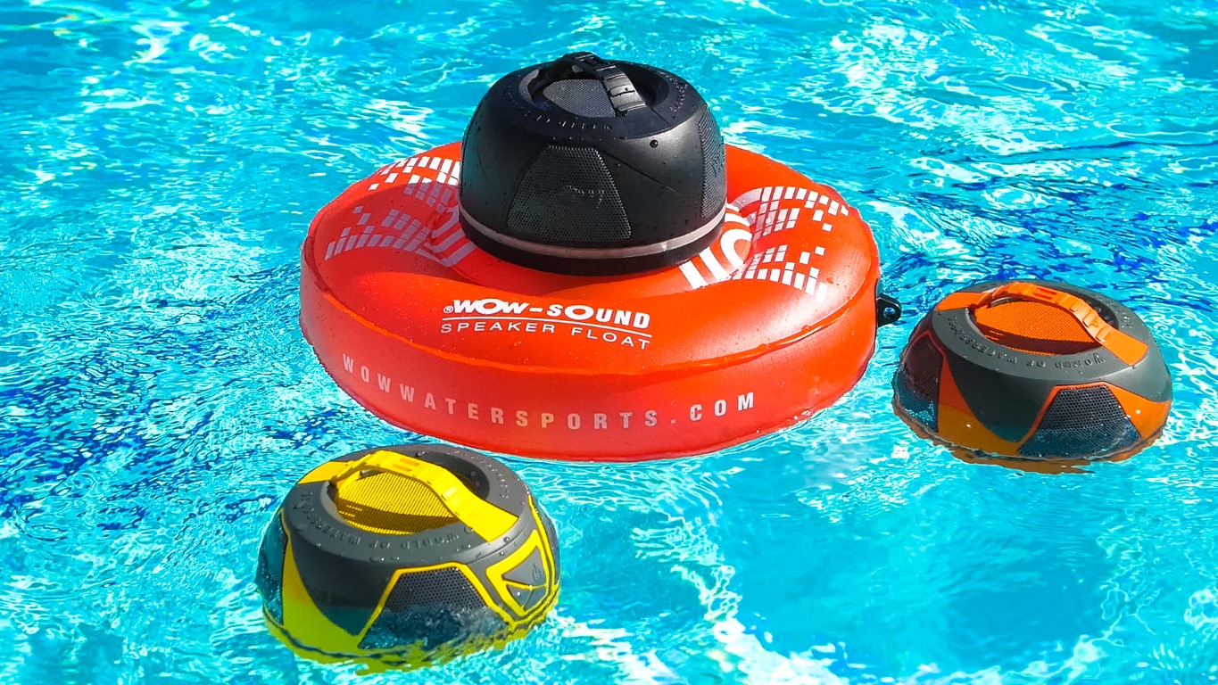 Three water sports helmets floating on a pool's surface, one on a red inflatable ring, others nearby, bright blue water background.