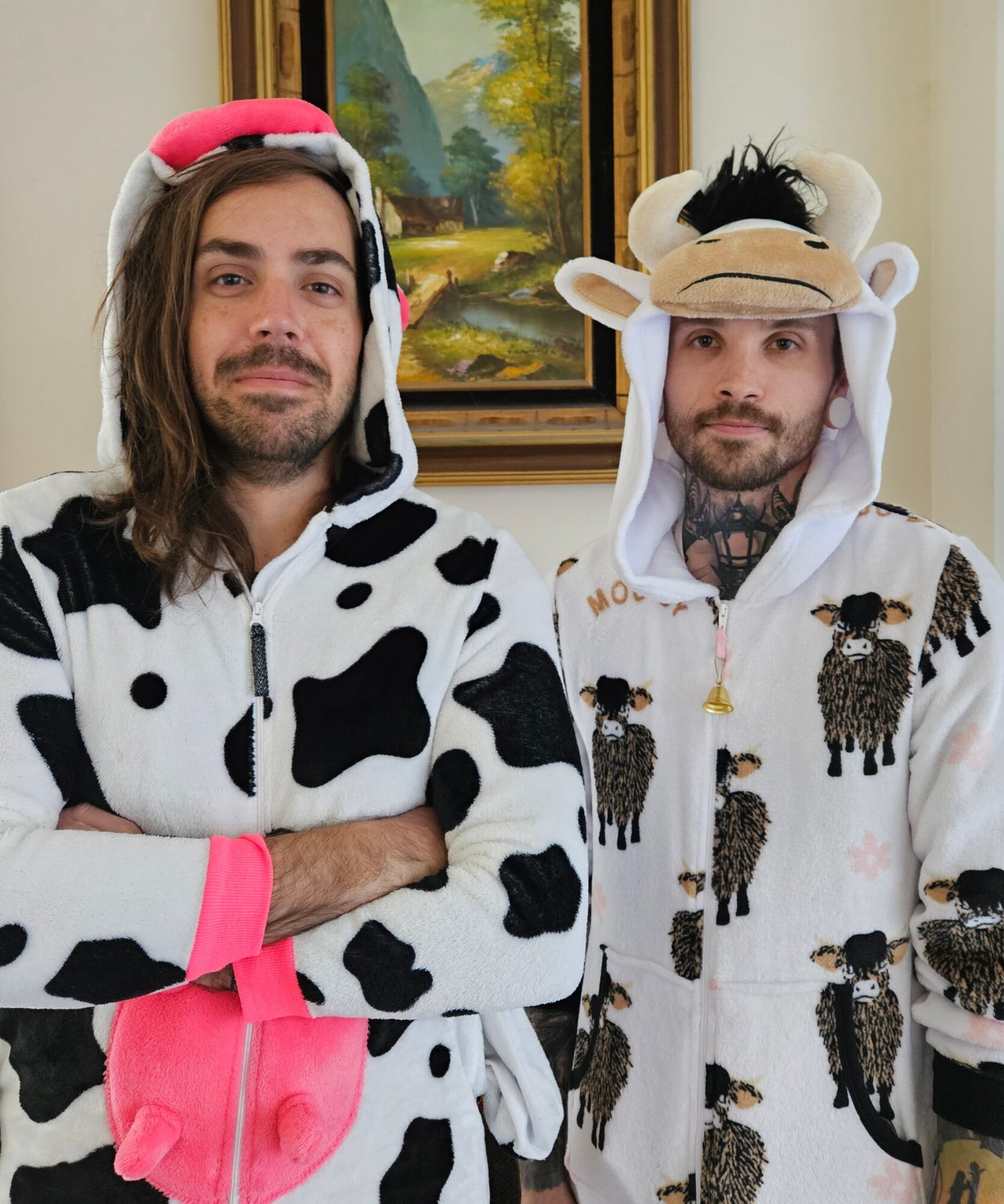 Two people in animal costumes, one dressed as a cow and the other as a lion, standing indoors in front of a painting.