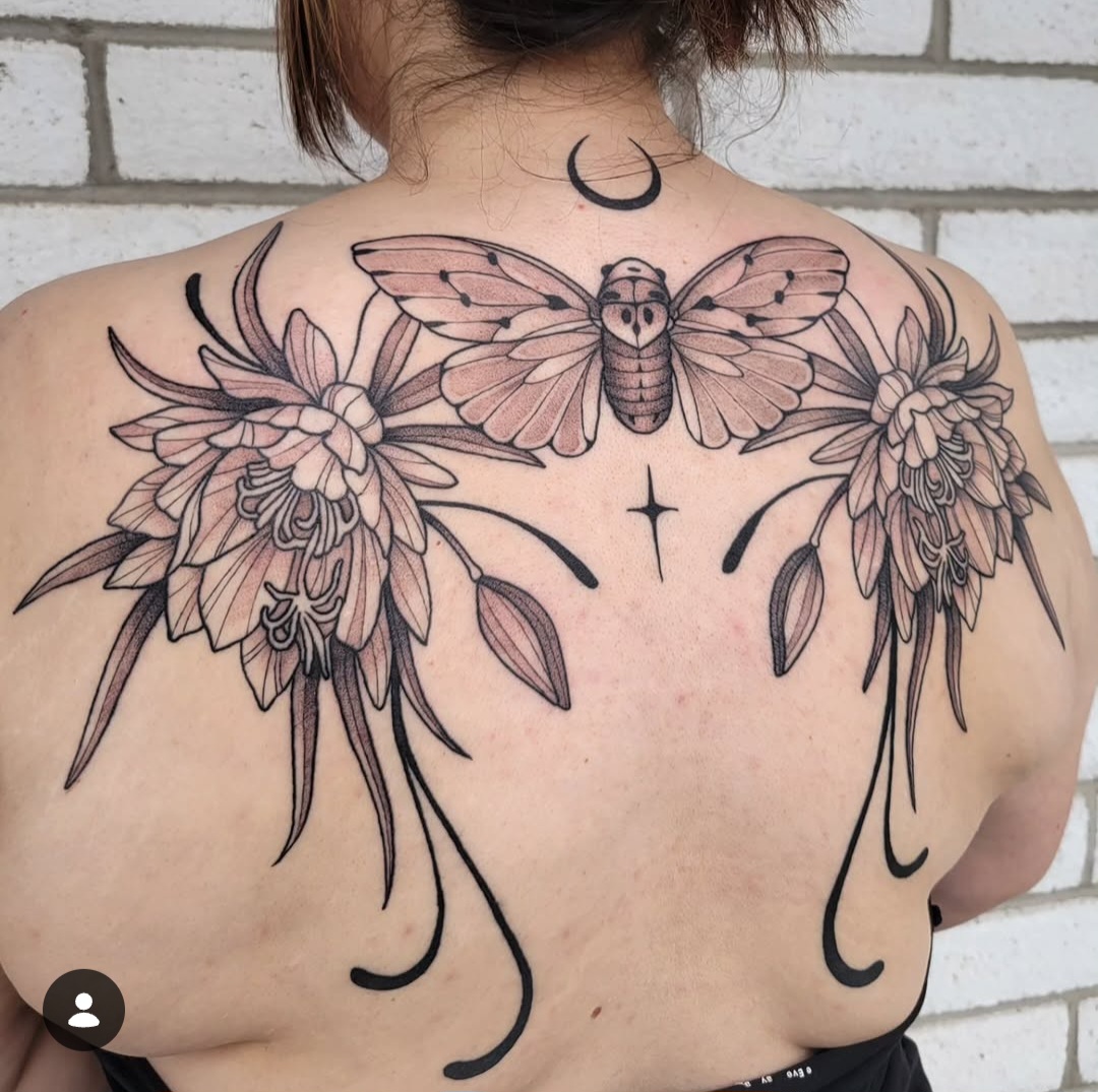 Tattoo of a moth, flowers, and abstract lines on person's upper back, with a crescent moon on neck. 20 words.