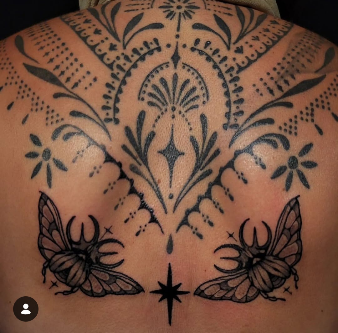 Tattoo with symmetrical floral and geometric patterns on upper back, two butterflies at bottom, and a star at center bottom.