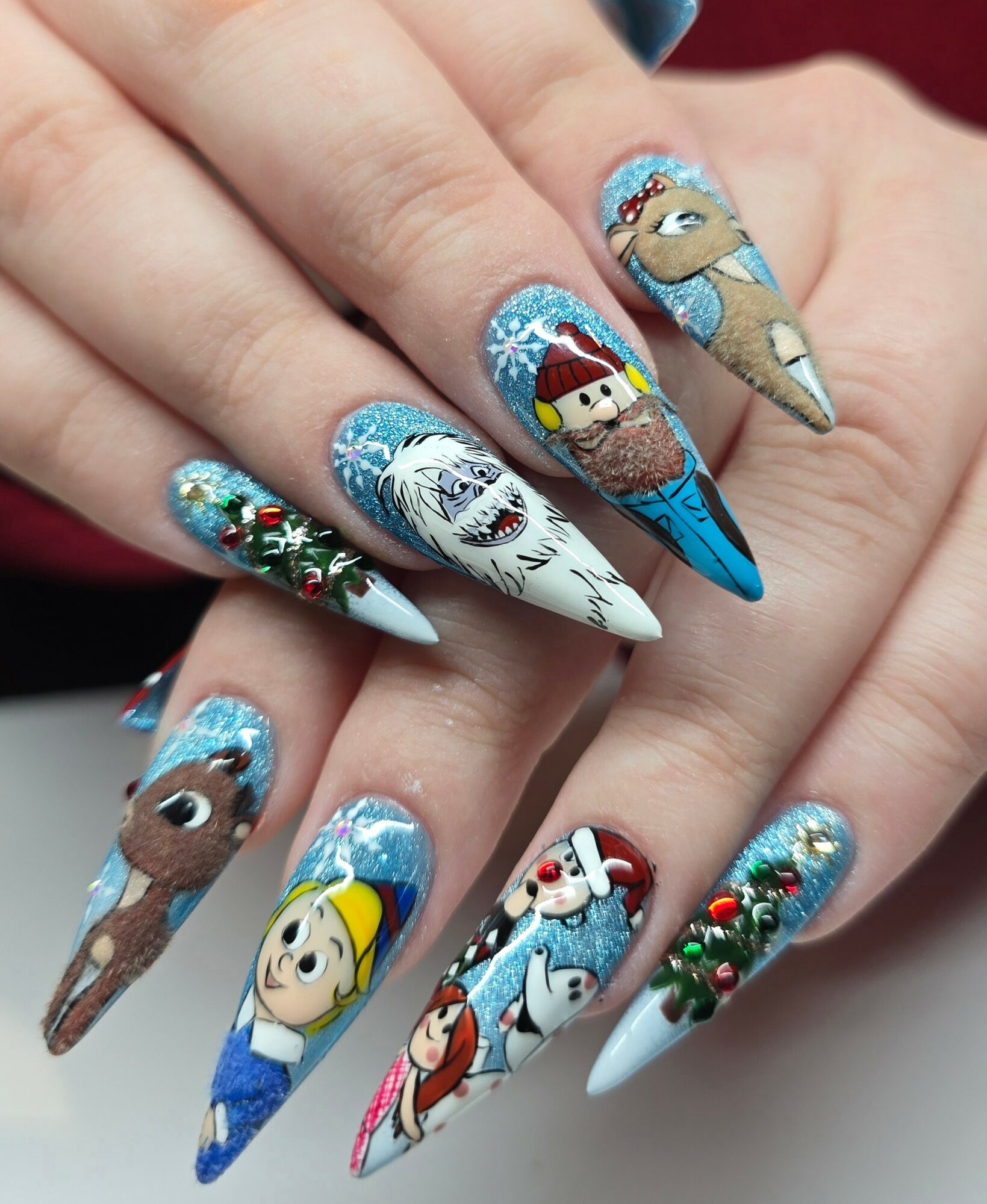 Nail art with Christmas and winter characters, including reindeer, snowman, and holiday decorations, on long, pointed nails.