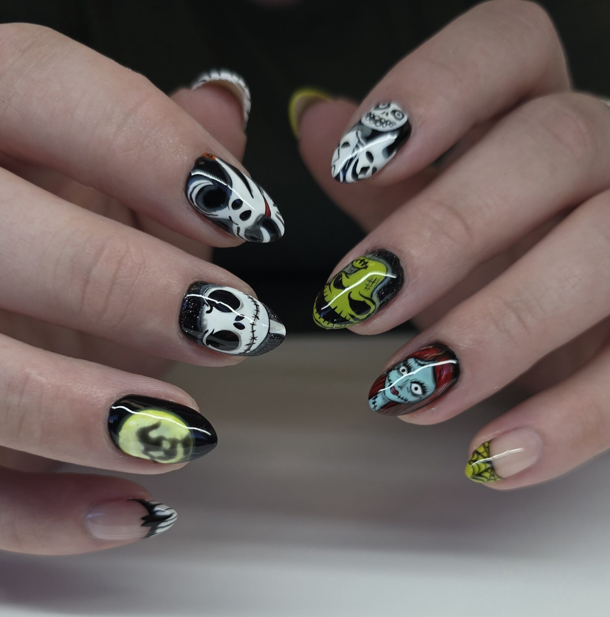 Close-up of hands with colorful, patterned nail art on fingernails, black, white, yellow, green, blue, and red designs.