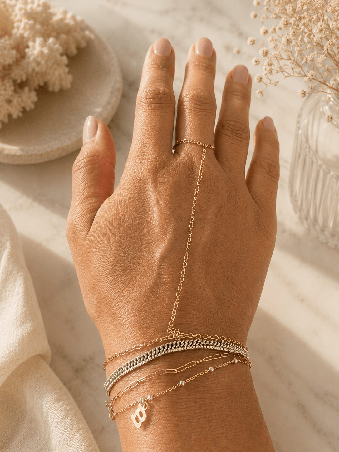 Hand with multiple bracelets and a ring, resting on a surface with decorative items nearby.