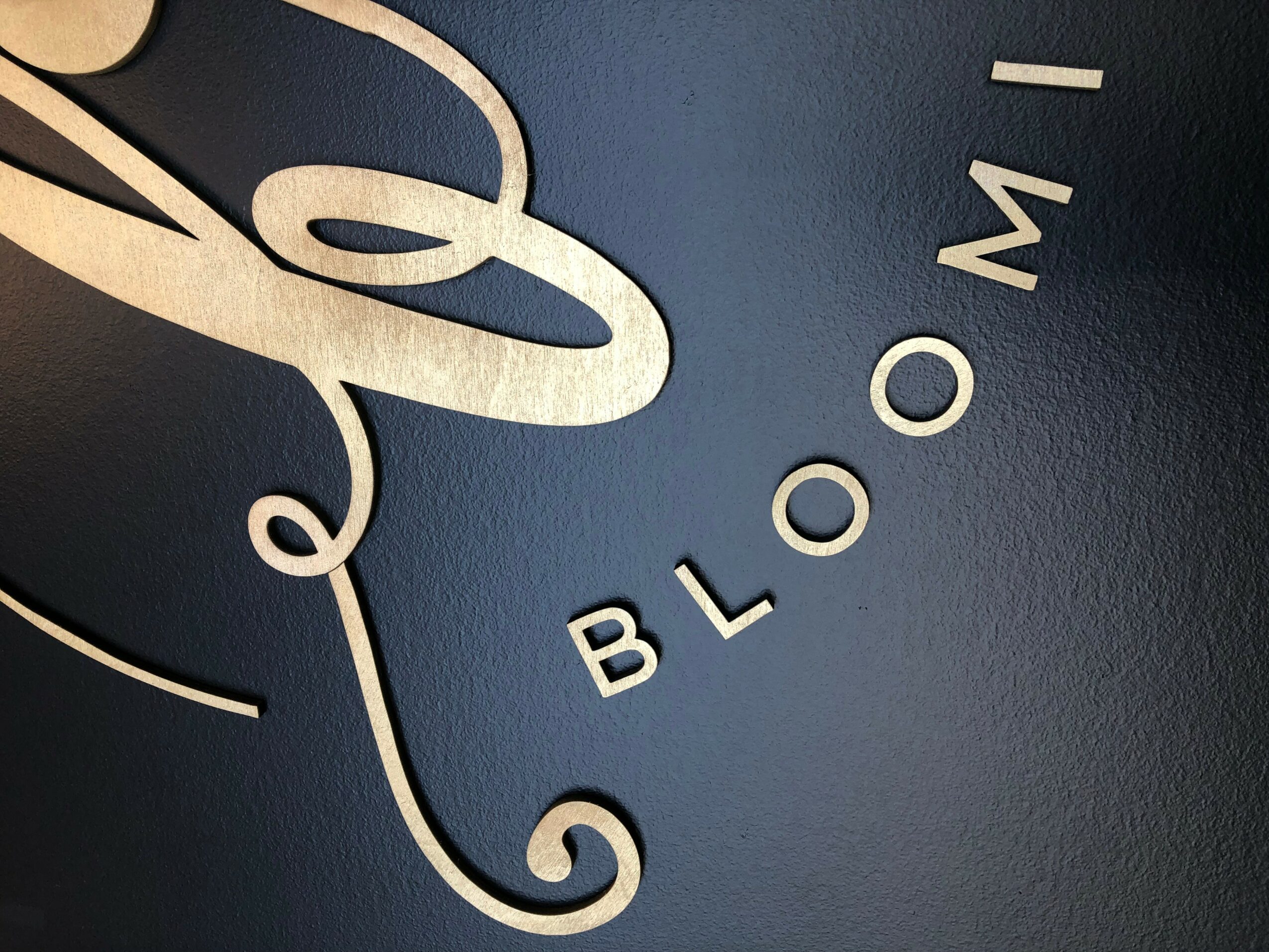 Close-up of a clock face with the word 'BLOOM' and partial clock hands, rotated 90 degrees clockwise.
