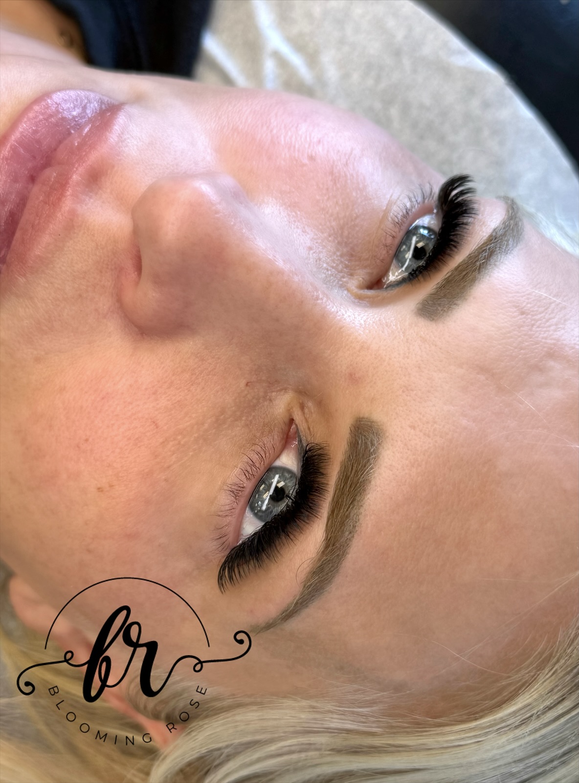 Close-up of a woman's face with makeup, focusing on her eyes and eyebrows, lying down with her head tilted back.